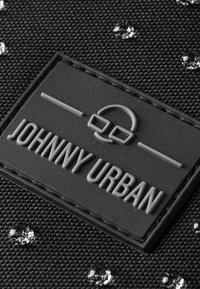 Tessuto nero testurizzato con un patch in gomma con il logo "JOHNNY URBAN" in rilievo e accenti riflettenti. Piccoli elementi riflettenti sparsi.