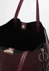 Sac cabas en cuir bordeaux avec une finition texturée, des ferrures dorées et un dessus ouvert. L'intérieur présente une doublure noire et une poche zippée.