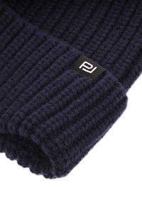 Ciemnoniebieska, dziergana czapka beanie z prążkowaną teksturą. Posiada małą czarną metkę z białym logo. Wykonana z miękkiego materiału, z możliwością złożenia mankietu.