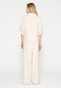 Creme-kleurige, zachte oversized top met opgezette mouwen, gecombineerd met wijd uitgesneden, hoogwaisted broek met zijzakken.