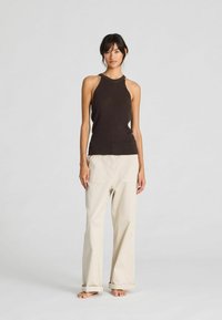 Top marrone senza maniche con colletto alto abbinato a pantaloni larghi beige chiaro con risvolti e due tasche frontali.