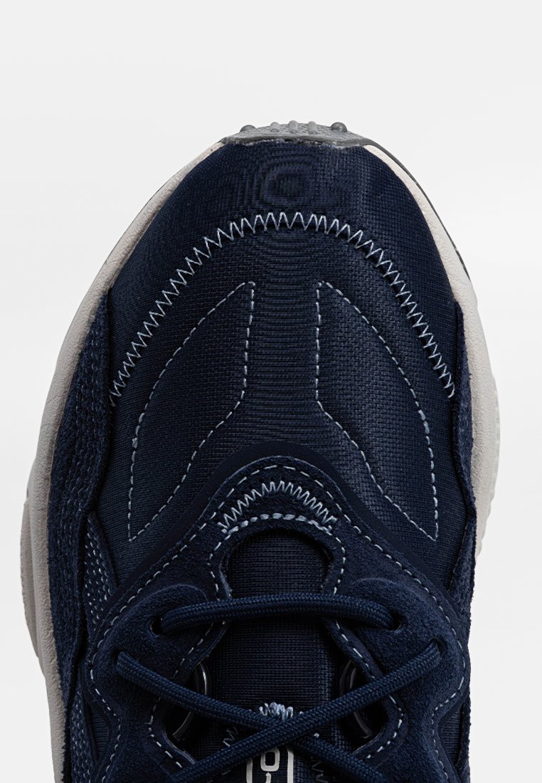 Sneaker blu navy con tomaia in tessuto testurizzato, cuciture bianche a contrasto, punta arrotondata e lacci piatti. Presenta una suola imbottita per il massimo comfort.