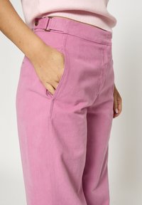Lyserøde bomuldsbukser med afslappet pasform, udstyret med sidelommer og lukning med metalknap. Stoffet har en blød tekstur.