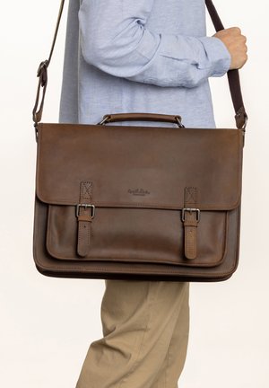 Brown leather messenger bag with a flat design, adjustable shoulder strap, and two buckled straps on the front. Textured surface, minimal branding.