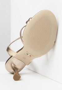 Sandaletta con tacco alto in metallo dorato, con sottile cinturino alla caviglia e suola rigata. Logo del marchio e taglia "37" stampati sulla suola.