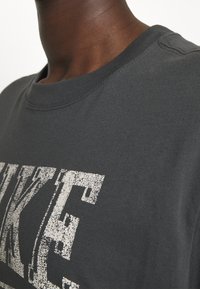 T-shirt en coton gris présentant un logo "NIKE" blanc usé sur la poitrine, avec un col ras du cou côtelé et des manches courtes.