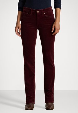 Widok na długość nóg osoby noszącej ciemnogranatowe spodnie ze sztruksu, ciemną bluzkę z długim rękawem i brązowe botki na prostym tle.