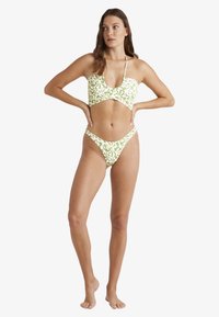 Zelená a bílá vzorovaná bikiny souprava s bandeau topem a vykrojením, skládající se z nízko vykrojených kalhotek. Vyrobeno z hladké, pružné látky.