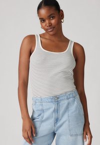 Top senza maniche a righe bianche e grigie, con scollatura a barca e spalline spesse, abbinato a pantaloni in denim azzurro chiaro a vita alta.