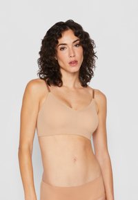 Nude wireless bra made from smooth fabric with a V-neck design, adjustable straps, and seamless edges for comfort.