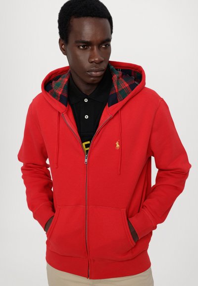 Sudadera roja con cremallera y forro de cuadros, cordones ajustables, bolsillos tipo canguro y pequeño logo bordado en el pecho.