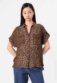 Leopardmönstrad skjorta i brunt och beige, kort ärm, med knäppning fram, två bröstfickor och en avslappnad passform. Slät tygtextur.