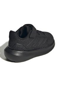 Svart atletisk sko med ett mesh-övre, texturerade detaljer och en vadderad krage. Säker remstängning med en solid gummisula.