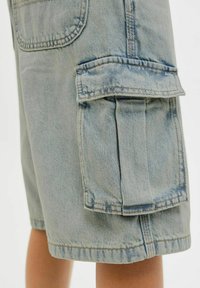 Shorts en denim bleu clair avec poches cargo, présentant une grande poche sur le côté, des coutures visibles et une coupe droite. Le tissu montre un léger délavage et une texture.