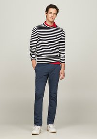 Maglietta a maniche lunghe a righe blu e bianche, colletto rosso, abbinata a pantaloni blu e sneakers bianche. Design semplice con colori a contrasto.