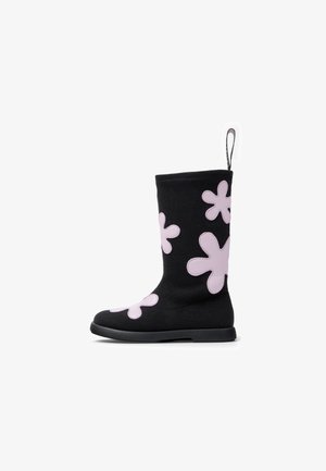 Stivale nero in maglia con gambale alto, caratterizzato da grandi applicazioni a forma di fiore rosa e suola in gomma nera. Include una linguetta nella parte superiore.