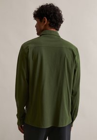 Tumerohelisest puuvillast pikakäistega särk, millel on klassikaline krae ja nööpidega mansetid. Sile tekstuur ja jahedalt istuv lõige on nähtavad tagant.