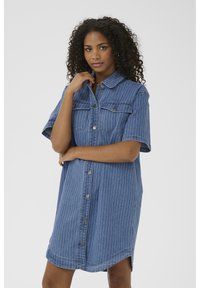 Jeansklänning med korta ärmar, knäppning med knappar, vertikala vita ränder, två bröstfickor och en lätt rundad nederkant.