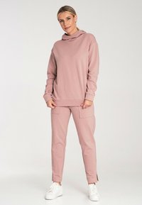 Różowy sweter z kapturem, sparowany z dopasowanymi spodniami cargo z bocznymi kieszeniami i szczelinami na kostkach, noszony z białymi sneakersami.