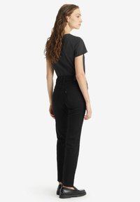 Camiseta de algodón negra de manga corta, combinada con jeans negros de tiro alto. El modelo lleva zapatos negros. Diseño minimalista, textura suave.