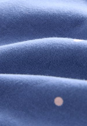 Tela azul con una textura suave, mostrando pliegues y un pequeño patrón de puntos de color claro. La superficie parece lisa y ligeramente aterciopelada.