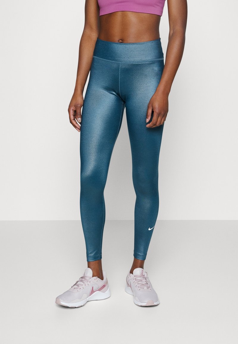 Leggings métalliques teal avec une taille haute et des coutures latérales, associés à des chaussures de sport Nike rose clair avec des accents blancs.