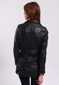 Svart läder trench coat med bälte i midjan, detaljerad sömnad och spetsig krage. Slät textur med en knappdetalj på baksidan.