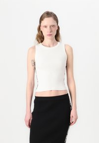 Hvit ribbet crop top med rund hals og sideakenter. Kombinert med et svart ribbet skjørt med en kontrasterende side logo-detalj.