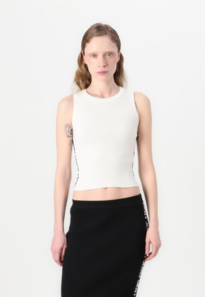 Top court en maille blanche avec un col rond et des accents sur les côtés. Associé à une jupe en maille noire avec un détail de logo contrastant sur le côté.