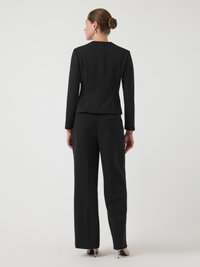 Svart skreddersydd dress med lange ermer, rett bukseben, glatt stoff, minimale sømmer og en strukturert silhuett.
