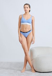 Σετ με ελαφρώς γαλάζιο σουτιέν bralette και στρινγκ με ελαστική ζώνη μέσης, με το λογότυπο Calvin Klein. Με απαλή υφή και εφαρμοστή σχεδίαση.