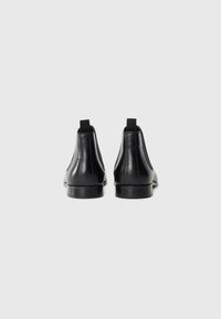 Botas de tobillo de cuero negro con paneles laterales elásticos, puntera redondeada y suela de goma plana. Incluyen una etiqueta de tiro para ponérselas fácilmente.