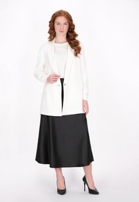 Blazer alb cu un singur nasture, asortat cu o fustă midi din satin negru și tocuri înalte negre. Material moale, design structurat și mâneci lungi.