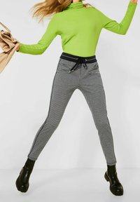 Green long-sleeve turtleneck top and black-and-white checkered leggings with side stripes. Black ankle boots complete the outfit.