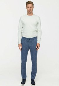 Lichtgrijze long sleeve shirt gecombineerd met gestructureerde blauwe sportbroeken met een elastische tailleband en trekkoord. Zwarte sneakers maken de outfit compleet.
