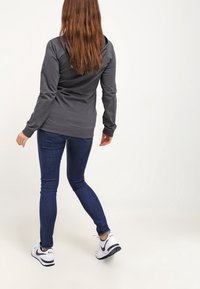 Felpa grigia con un design aderente, polsini a coste abbinati e dettagli cuciti sul retro, abbinata a jeans slim blu scuro e scarpe da ginnastica bianche.