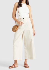 Crème-kleurige wijde broek gemaakt van textuurstof, gecombineerd met een witte scalloped haltertop en bruine sandalen met bandjes, met een ronde geweven tas.
