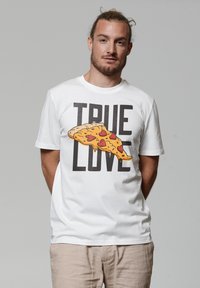 Weißes Baumwoll-T-Shirt mit einem Grafiktbild einer Pizzastücke mit herzförmigen Belägen und dem Text "TRUE LOVE" in fetten schwarzen Buchstaben.