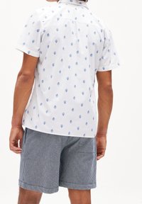 Camicia bianca a maniche corte con motivo a foglie blu, abbinata a pantaloni corti a strisce grigie e bianche. Presenta un colletto.