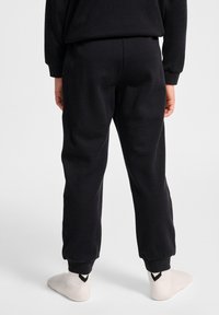 Zwarte sweatpants met elastische boorden, gemaakt van zachte stof. Ze hebben een relaxte pasvorm en worden gecombineerd met lichte sokken met een donker logo.