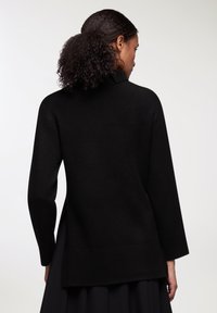 Czarny sweter dziany z wysokim kołnierzem, długimi rękawami i ribbowymi mankietami. Projekt charakteryzuje się nieco dłuższym tylnym dołem, co tworzy luźny krój.