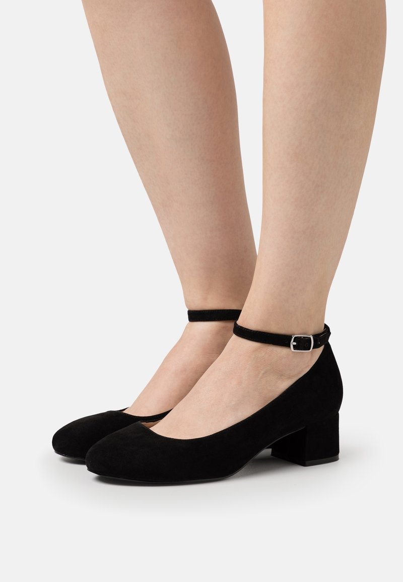 Černé semišové boty na blokovém podpatku s kulatou špičkou a kotníkovým páskem s malou stříbrnou sponou. Měkká struktura a minimalistický design.