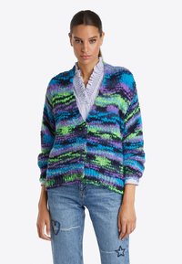 Un cardigan en tricot coloré avec des rayures vertes, bleues et violettes, présentant un devant boutonné, une coupe oversize et un tissu texturé.