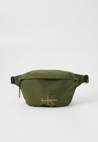 Marsupio verde in nylon con chiusura zip, tracolla regolabile e logo Calvin Klein dorato. Texture liscia, design leggero.
