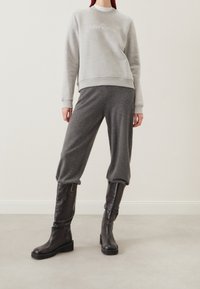 Šedá mikina s texturovaným povrchem a manžetami, zkombinovaná s volnými šedými kalhotami. Černé kožené boty s nízkými blokovými podpatky.