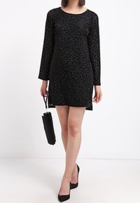 Svart leopardmönstrad klänning med långa ärmar, rund halsringning och rak skärning. Matchad med svarta högklackade skor och en liten handväska.