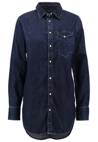 Mörk denimskjorta med långa ärmar, kn äppning fram, krage och en bröstficka. Har en rundad nederkant och vita knappar för knäppning.