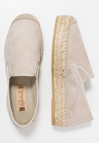 Beżowy espadryl z miękką zamszową cholewką, elastycznymi bocznymi panelami, oplecioną lamówką z juty i gumową podeszwą. Lekko spłaszczony.