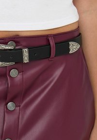 Burgundská sukně z umělé kůže s černým páskem zdobeným ornamentálními stříbrnými akcenty a kovovými knoflíky, hladká textura a přiléhavý střih.