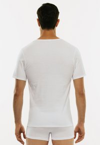 T-shirt bianco a maniche corte realizzato in tessuto morbido, con collo tondeggiante e una texture liscia, mostrato da dietro.